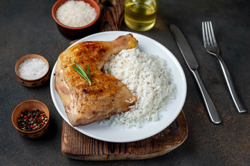 grilled chicken leg with spices and rice on a white plate on a stone background