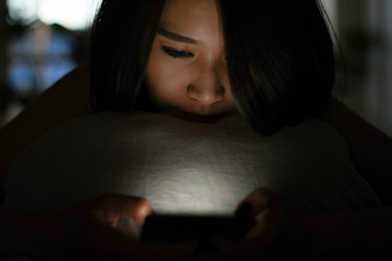 Beautiful lonely woman sleepless chat play game or use social media mobile app with smartphone in the dark late night on the bed while self quarantine and stay home to avoid covid19 virus infection