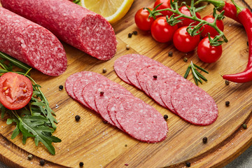 Traditional thinly sliced salami on a wooden cuttingboard  with spices, lettuce, avocado and tomatoes. Cold meat plate