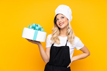 Teenager girl pastry holding a big cake isolated on yellow background laughing and looking up