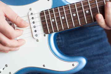 Close-up of man playing blue and white electric guitar