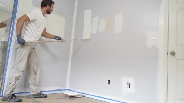 Painter man painting the wall in home, with paint roller and white color paint. Room renovations at house.