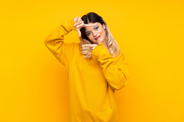 Teenager girl isolated on yellow background focusing face. Framing symbol