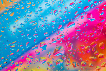 Water droplets on a glass above colorful diagonal background of blue, pink, red, orange and yellow colors