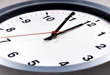 Fototapeta premium It is five to twelve, the clock is ticking. Modern white grey clock shows the time 5 before 12. Close up to a wall clock, with five minutes to twelve o'clock. Time is running out 
