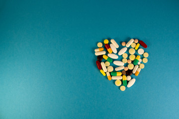 Macro shot of colorful tablets and capsules in shape of heart on blue background