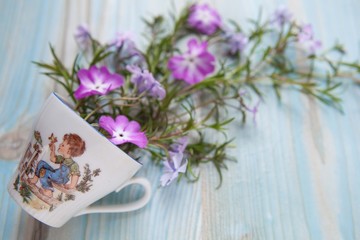 Spring concept. Floral background. Cup with pink and violet flowers on a blue wooden background. Space for text