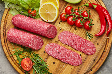 Traditional thinly sliced salami on a wooden cuttingboard  with spices, lettuce, avocado and tomatoes. Cold meat plate