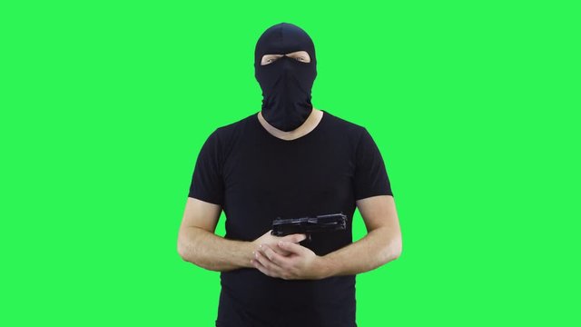 A man in a balaclava says to the camera holding a gun in his hands then makes a headshot.Temple shot.Green screen background.