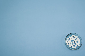 White pills in the glass bowl on blue background on the right side