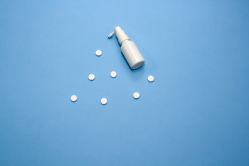 White pills with white bottle of spray on blue background