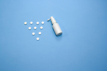 White pills with white bottle of spray on blue background