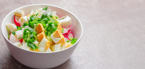 Fresh salad with egg, radish and herbs in a deep plate on the table