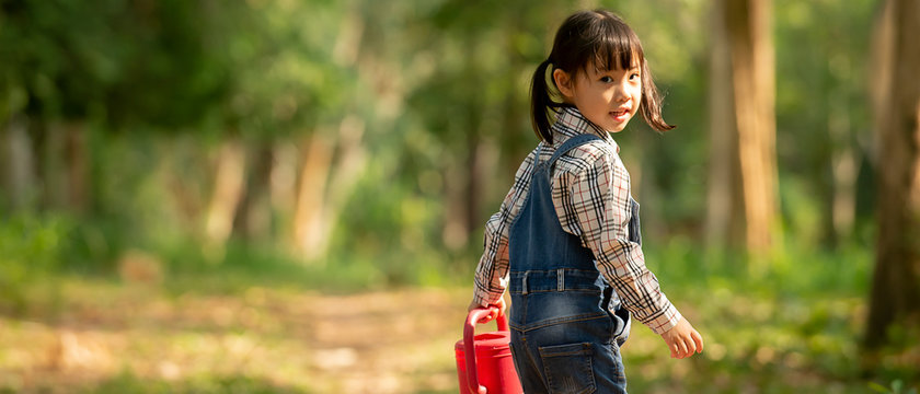 Happy cute asian little girl holding watering can walking  in to park