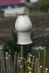 An old Russian-style pot is turned upside down and hangs on a fence of thick branches. Photos of...