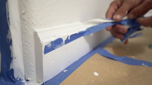 Removing masking tape from molding. A painter pulls of blue painter's tape from the wall to reveal a clean edge baseboard.