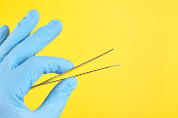 Hand of doctor in blue medical glove holding a tweezers isolated on yellow background