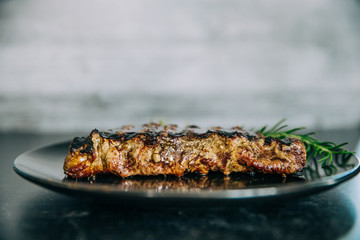 Side view of a single sirloin cut steak that has been grilled outdoors on a gas grill with a fork and knife with a sprig of rosemary