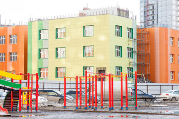 An empty children's playground with swings, a slide and horizontal bars of different colors in the courtyard of a kindergarten in a city landscape in self-isolation and quarantine mode.