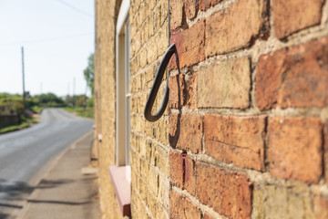 Shallow cable of a thick mains power cable entering a hole in a brick built house, seen on a rural street. The cable is looped and the hole filed in.