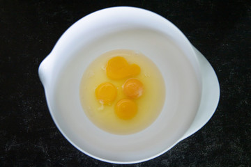 4 eggs cracked open with the yolk and the egg white inside with 3 whole yolks and one broken one