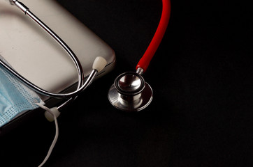 Stethoscope, face mask and red heart with laptop on dark background. Health concept. Selective focus.