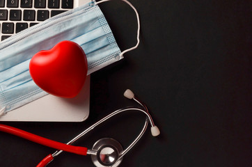 Stethoscope, face mask and red heart with laptop on dark background. Health concept. Selective...