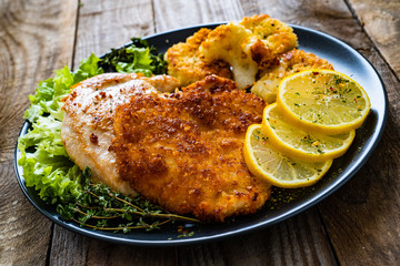 Pork chops with fried cauliflower and vegetable salad on wooden background
