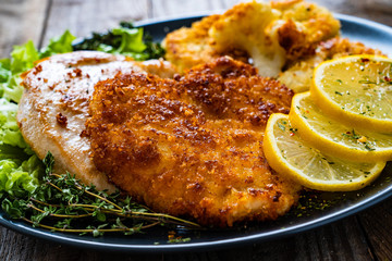 Pork chops with fried cauliflower and vegetable salad on wooden background