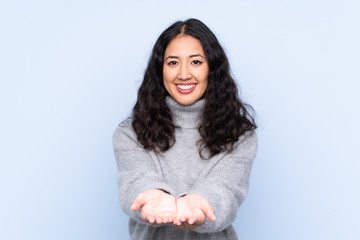 Spanish Chinese woman over isolated blue background holding copyspace imaginary on the palm to...