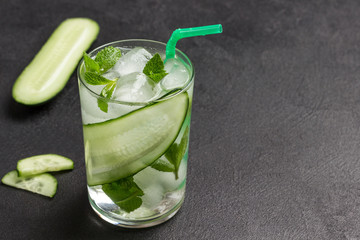 Cooling summer drink with ice and slices of cucumber. Mint and chopped cucumber on black background