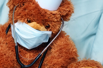 Portrait of tired teddy bear doctor with protective medical mask and stethoscope. Teddy bear sits...