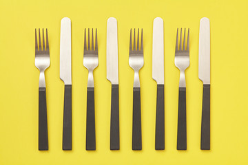Black knife and fork on yellow background. Top view