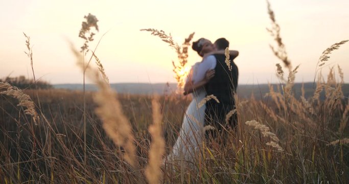Romantic date millennium wedding couple on spikelet field at sunset in autumn background. A bride in wedding dress is hugging with her beloved groom on the nature outside. Vacation newlyweds outside.