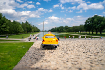 Yellow taxi model in Washington city with Washington memorial in the background.