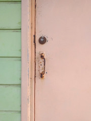 Close-up of pale pink rusty Caribbean house door, door handle, lock and light green wooden facade. Tropical Construction and Architecture. Martinique, Antilles. French West Indies.
