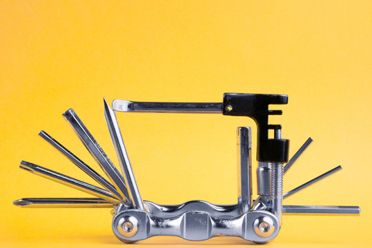 Old metallic unfold bike multi tool set with chain remover on a yellow background. Bicycle multifunction hand tool.