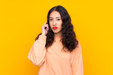Spanish Chinese woman over isolated yellow background having doubts