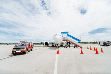 A Boeing prepared for departure to the airport on Bali, trucks all around. Front view of airplane during maintenance. Sunny afternoon at Tambolaka West Sumbawa Airport.