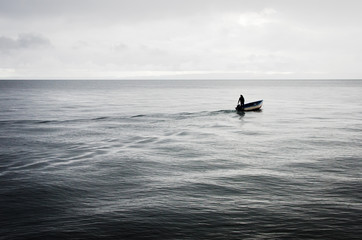 Pescador navegando mar adentro en una pequeña barca en un día gris y lluvioso