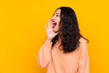 Spanish Chinese woman over isolated yellow background shouting with mouth wide open to the lateral