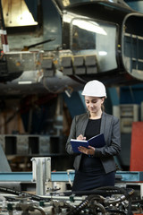 Portrait of a female factory manager in a white hard hat and business suit. Controlling the work process at the airplane manufacturer. 