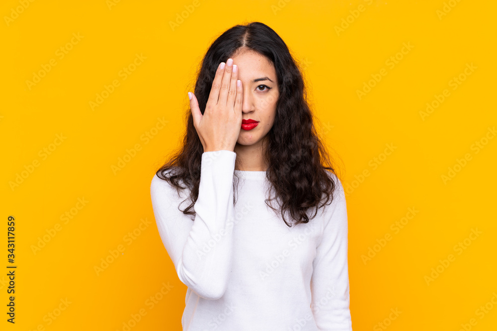 Wall mural mixed race woman over isolated yellow background covering a eye by hand