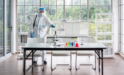 Asian man wear personal protective suits or PPE, goggle, and face mask, making disinfection and decontamination on science and microbiology lab room. Covid-19, laboratory and disinfection concept