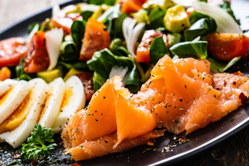 Salmon salad - smoked salmon, boiled eggs and vegetables on wooden background

