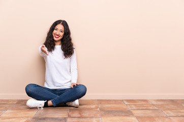 Young woman sitting on the floor shaking hands for closing a good deal