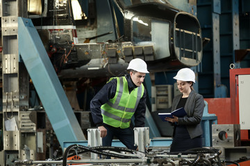 Portrait of a female factory manager in a white hard hat and business suit and factory engineer in...
