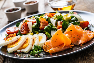 Salmon salad - smoked salmon, boiled eggs and vegetables on wooden background
