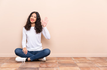Young woman sitting on the floor saluting with hand with happy expression