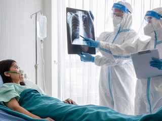 Two asian doctor wear PPE suit with N95 mask and faceshield, examine pulmonary chest x-ray film from coronavirus infected patient in negative pressure room. Coronavirus, medical and covid19 concept